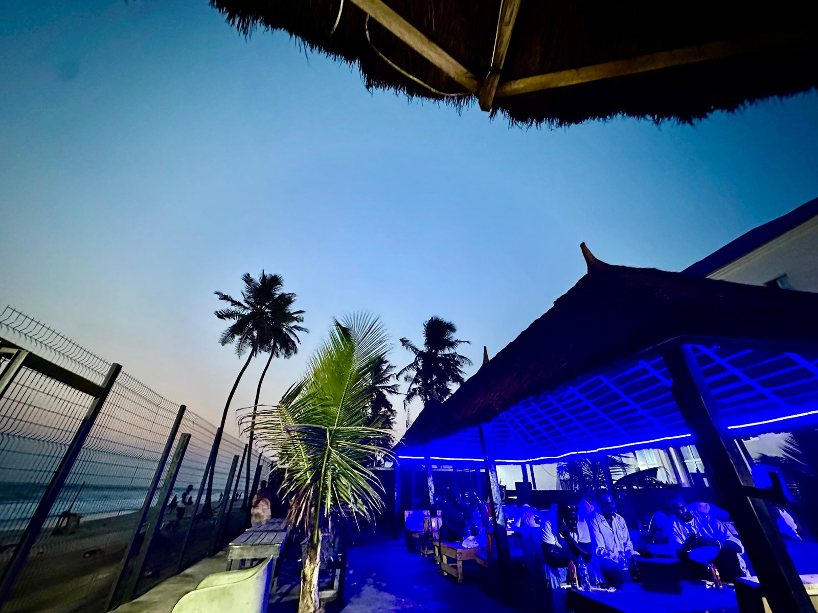 The beach bar glowing blue under thatch roofs at twilight